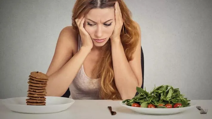 Mujer ante la mesa decidiendo entre galletas y una ensalada
